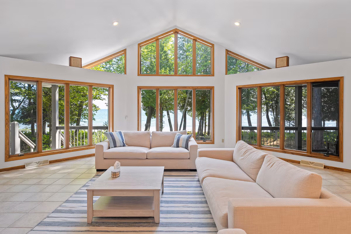 Bright living room with vaulted ceilings and panoramic lake views through floor-to-ceiling windows